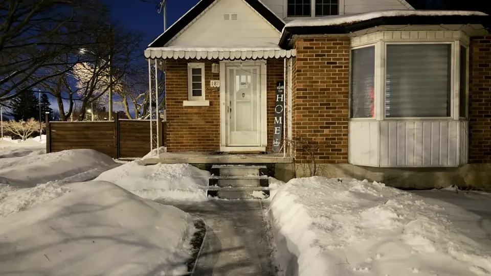 Snow-lined path leading to a brick house entrance at night