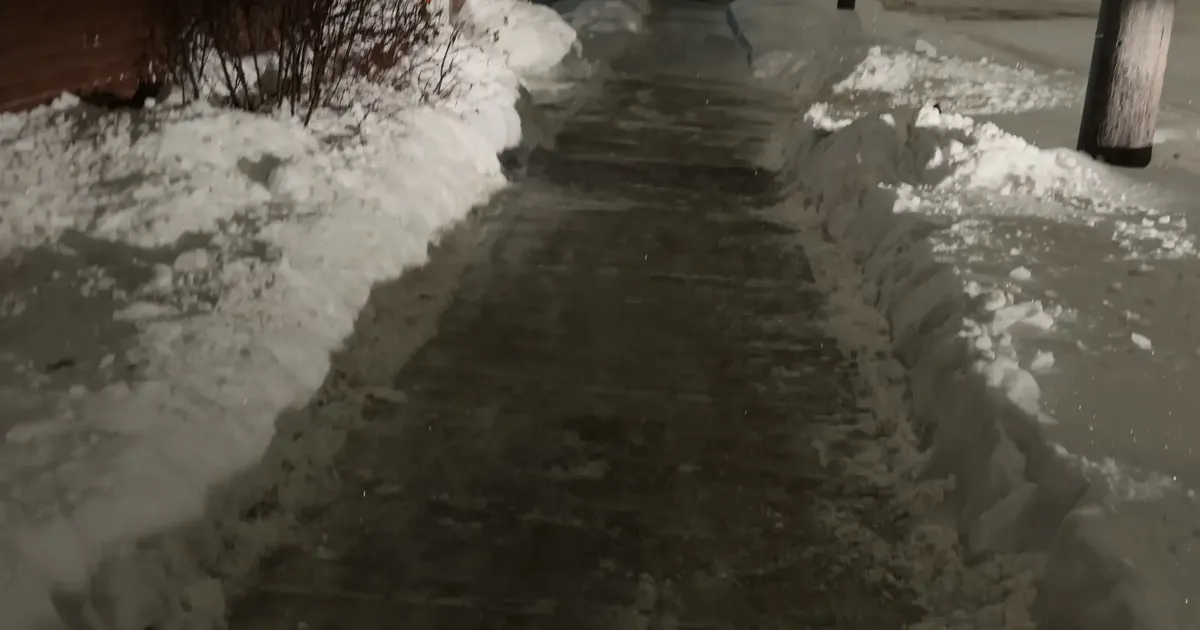 Dark wet-looking walkway bordered by packed snow at night